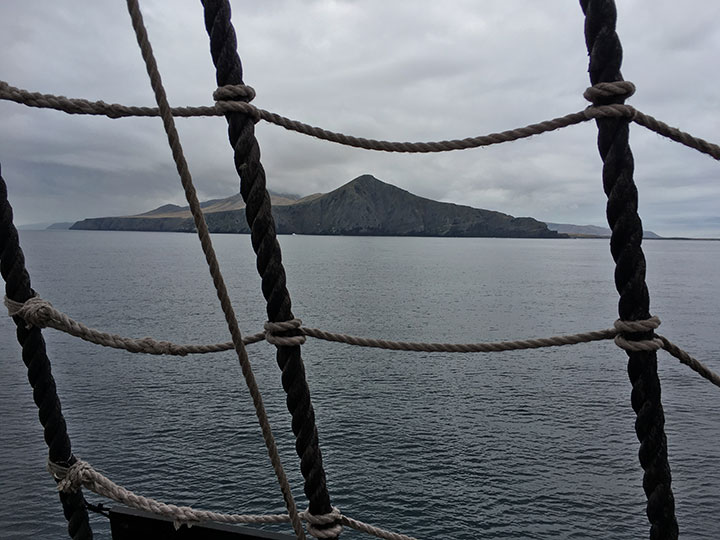 view of pointed hills on the shoreline through rope boat rigging